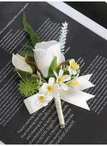 Macro detail of white silk rose boutonniere with satin bow and green leaf accents