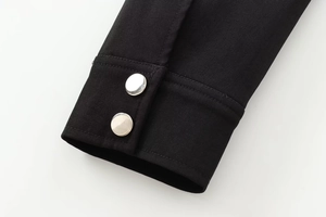 Detail of black twill jacket cuff with dual silver metal buttons and fine fabric texture