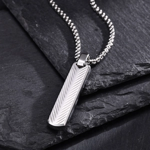 Close-up of silver long bar pendant with chevron patterns on a dark stone surface
