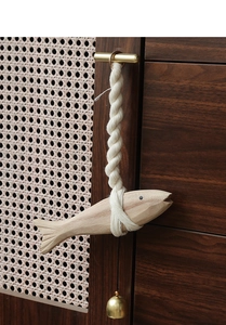Detail of wooden fish hanging decor with cotton rope and golden bell on wicker furniture