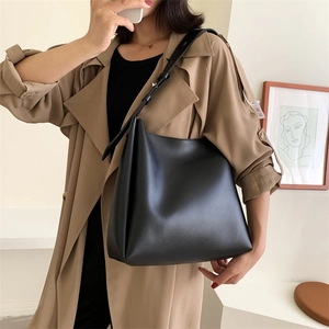 Black large-capacity leather tote bag with adjustable strap worn by a model in interior