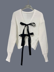 Dettaglio del cardigan in maglia bianca con fiocchi neri e trama in evidenza