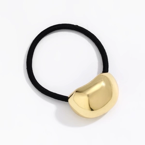 Detailed close-up of a minimalist gold bean-shaped charm on a black elastic hair tie