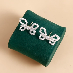 Close-up of handmade woven pearl bow earrings on a dark green velvet display stand