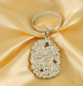 Macro detail of silver stainless steel dragon relief keychain on golden silk fabric