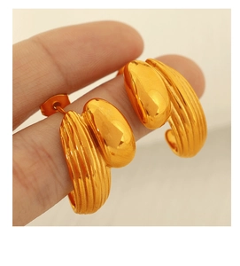Detail of C-shaped gold heart earrings with mixed smooth and textured finishes on finger