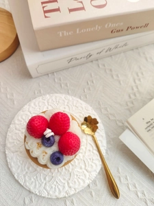 Detailed close-up of strawberry and blueberry cake scented candle on a lace napkin