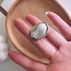Detail of a gold irregular geometric ring with a baroque pearl on a wooden tray