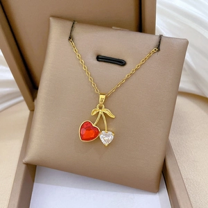 Detail of gold cherry necklace with red and clear heart-shaped crystals on white silk