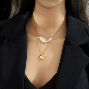 Double-layered gold necklace with heart pendant and pearls on a model wearing black suit