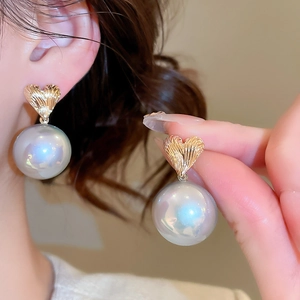 Detail of heart-shaped gold earrings with large iridescent pearls worn by a model