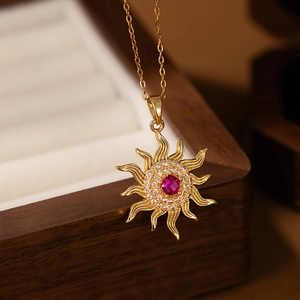Macro detail of sun pendant with red gemstone and white zircon in golden stainless steel
