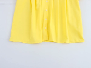 Detailed close-up of yellow doll collar blouse featuring white buttons and pleated fabric