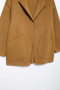 Detail view of camel wool coat showing large patch pockets and premium fabric texture