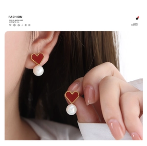 Detail view of model wearing gold heart earrings with elegant white pearls and red enamel