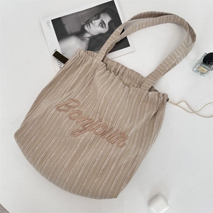 Detail of khaki striped tote bag with Bonjour embroidery and side drawstring closure