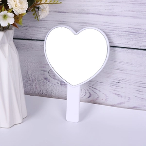 Cute white heart-shaped handheld mirror with ergonomic handle on a minimalist vanity