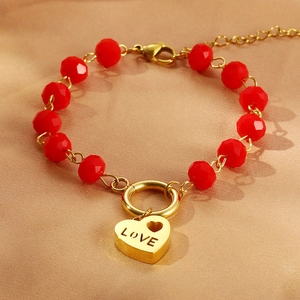 Dettaglio di perle sfaccettate rosse e ciondolo a cuore dorato inciso LOVE sul bracciale