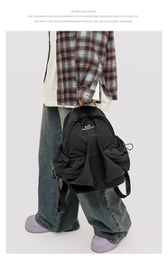 Detail of a black space-themed backpack being held by a model in a casual street outfit