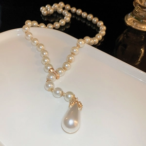 Detail view of a Y-shaped pearl necklace with a gold water drop pendant on a white plate