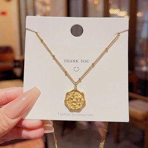 Close-up of gold stainless steel necklace with a vintage floral embossed coin pendant
