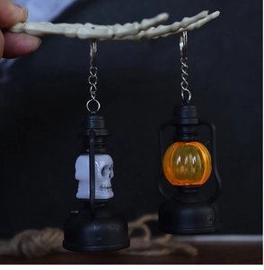 Detail of Halloween LED skeleton and pumpkin lantern keychains held by a skeleton hand