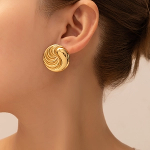 Close-up of a model wearing chunky gold spiral disc earrings with a high-polished finish