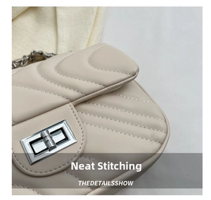 Close-up of wavy quilted stitching and silver twist lock on cream leather crossbody bag
