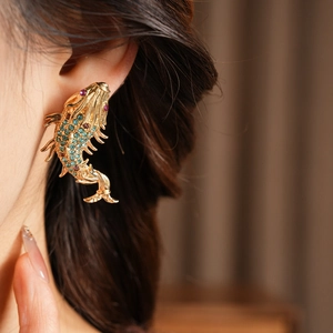 Macro shot of gold fish earrings with blue rhinestones and pink accents on model
