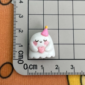 Close-up of a white resin ghost figurine with pink heart and party hat on scale mat