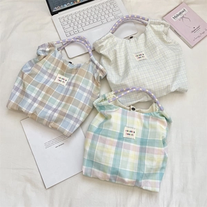 Sacs cabas en toile à carreaux avec poignées fleuries posés sur du linge blanc