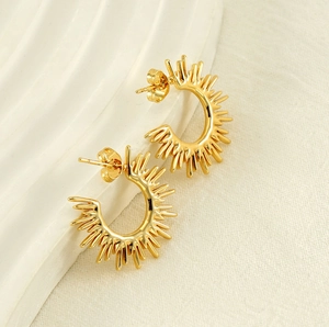 Close-up of golden sunray fan-shaped earrings on textured ceramic and fabric