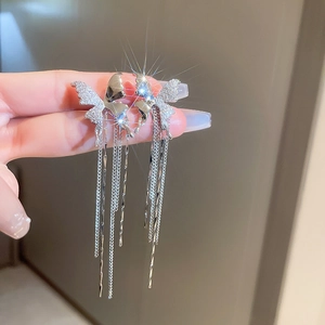 Gros plan d'un ear cuff papillon argenté avec glands en strass brillants tenu à la main