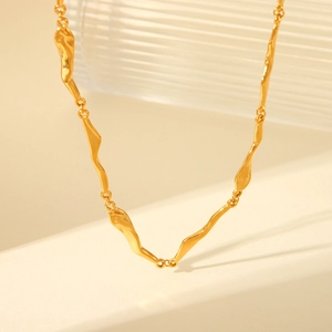Detailed shot of gold wave-link necklace on a textured surface with soft lighting