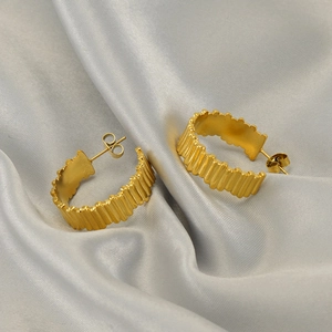 Golden ribbed hoop earrings in geometric gear design on soft light grey silk fabric