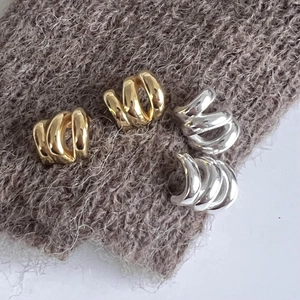 Detail of gold and silver minimalist C-shaped wavy hoop earrings on grey knit fabric