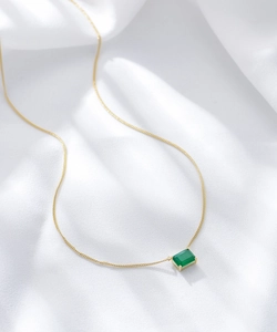Detailed view of square emerald green gemstone on a gold s925 silver necklace on silk