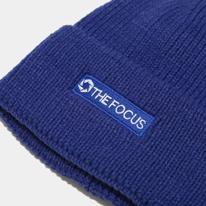 Detailed view of the dark blue ribbed knit beanie with THE FOCUS embroidered label