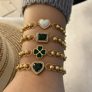 Detailed view of four-piece gold bracelet set with emerald green stones and heart charms