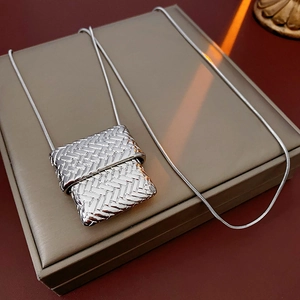 Macro detail of a silver woven purse pendant on a fine snake chain necklace