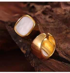 Detail of wide gold plated titanium rings with white shell inlay on a textured wood block