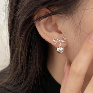 Close-up of elegant silver bow and heart dangle earrings worn on a woman's ear
