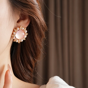 Gros plan de boucles d'oreilles vintage soleil avec perles et opale rose sur l'oreille