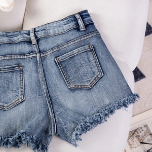 Dettaglio di pantaloncini in denim azzurro con orlo sfrangiato e tasca posteriore su sfondo