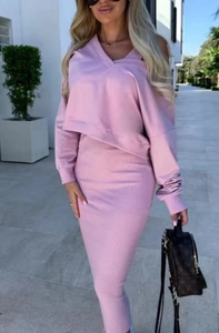Outdoor street view of a woman wearing a pink V-neck knit sweater and matching midi skirt