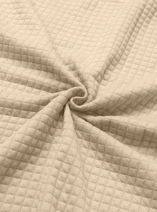 Close-up of beige waffle knit fabric with a diamond quilted pattern and soft texture