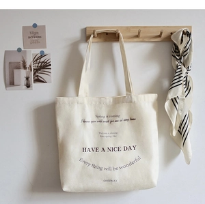 Close-up of beige canvas tote bag with black print hanging on a wooden wall hook