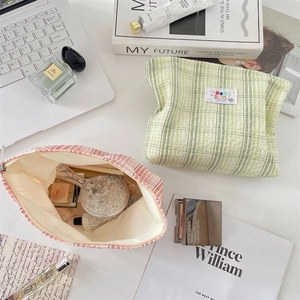 Flat lay of plaid cosmetic pouch with pastel grid pattern on desk with lifestyle props