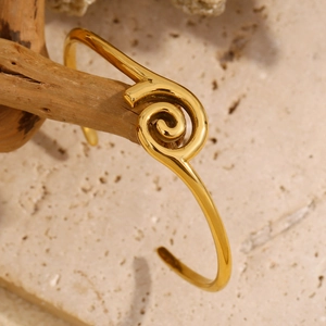 Macro shot of 18K gold plated spiral cuff bracelet on minimalist beige stone surface