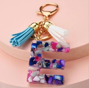 Macro view of resin letter E keychain with colorful stone chips and blue tassels